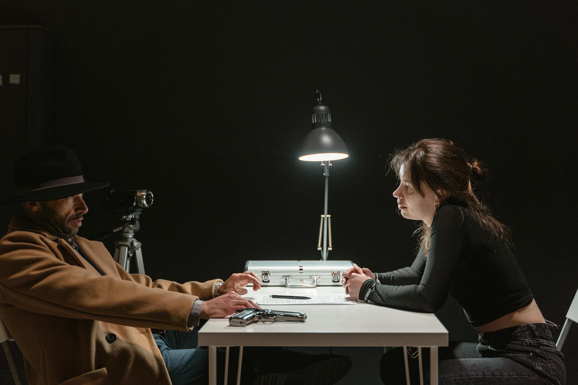 Tense interrogation scene with a man and woman in a dark room under harsh lighting.